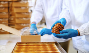 Two hard working food plant employees in sterile uniforms packing cookies in boxes.